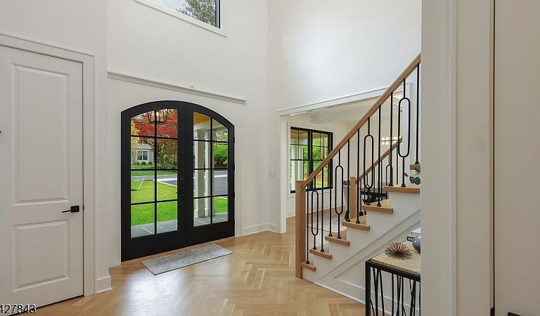 Two-story foyer with herringbone hardwood floors, arched glass entry door, and an open staircase with custom wrought iron balusters.