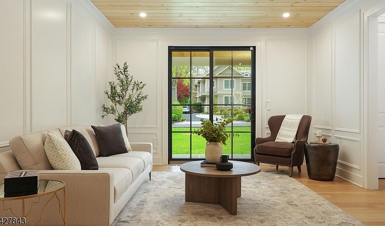 Sophisticated living room with wood-planked ceiling, classical wall paneling, and tall glass sliders opening to the front porch.