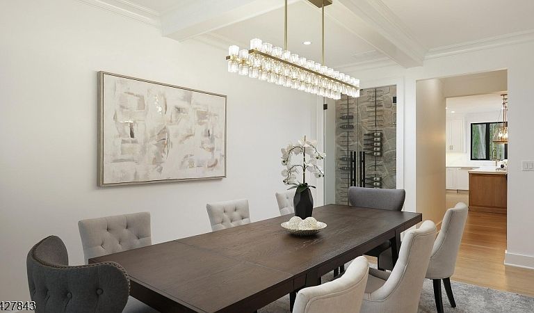 Formal dining room with coffered ceiling, a linear crystal chandelier, and a glass-doored wine display set into a stone-clad wall.